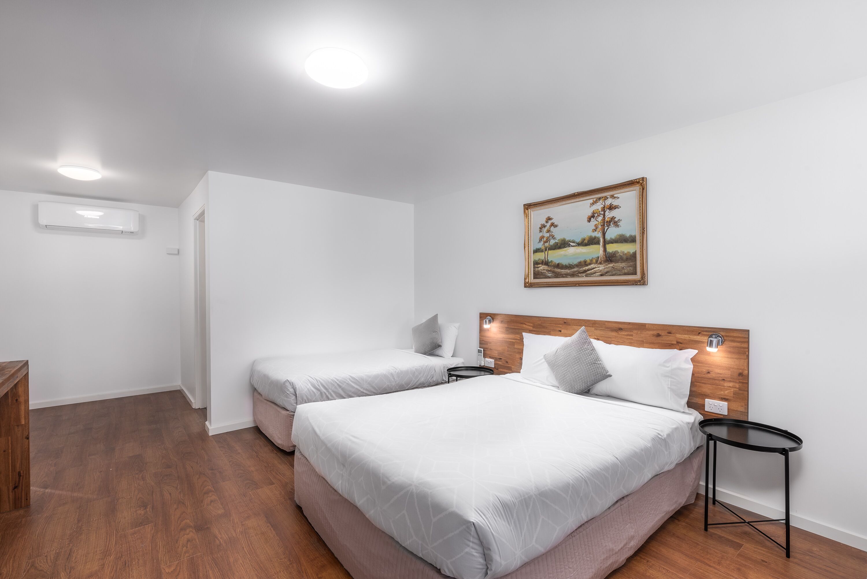 Une chambre d’hôtel avec deux lits, une tête de lit en bois, une petite table de chevet et une commode, ainsi qu’un tableau accroché au mur.