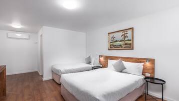 Une chambre d’hôtel avec deux lits, une tête de lit en bois, une petite table de chevet et une commode, ainsi qu’un tableau accroché au mur.