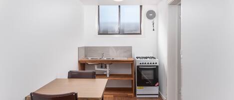 Una cocina compacta con una mesa de madera, sillas, estufa y una ventana.