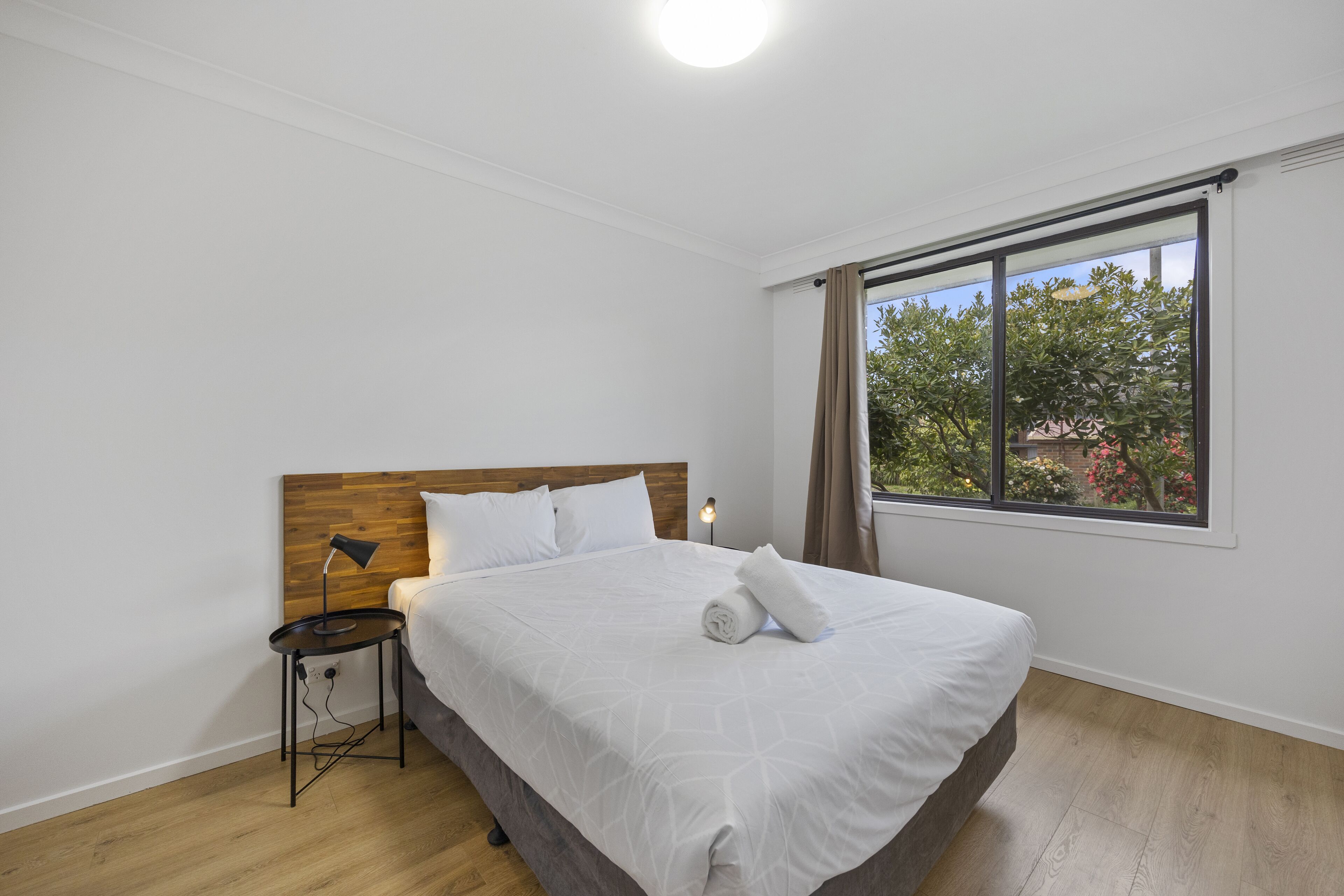 A neatly made bed with white linens, a wooden headboard, and a bedside table with a lamp.