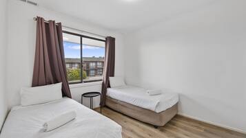Una habitación de hotel con dos camas, una mesita y un ventanal con cortinas.