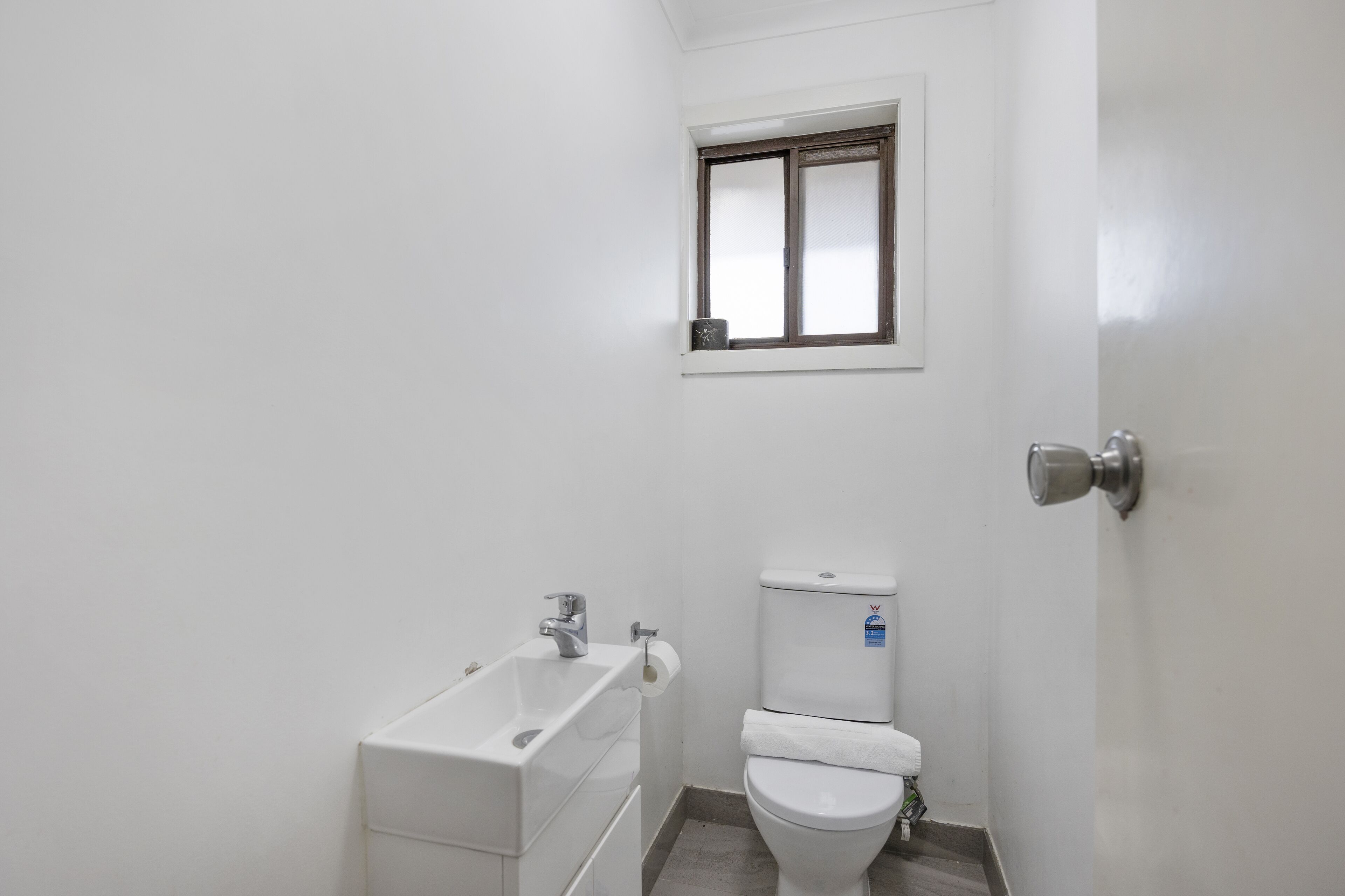A small, white bathroom with a toilet, sink, and window.