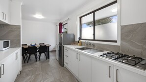 Una cocina moderna con armarios blancos, un refrigerador de acero inoxidable, una estufa a gas y un ventanal que deja entrar luz natural.