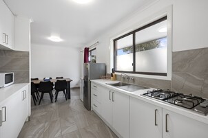 A modern kitchen with white cabinets, a stainless steel refrigerator, a gas stove, and a window providing natural light.