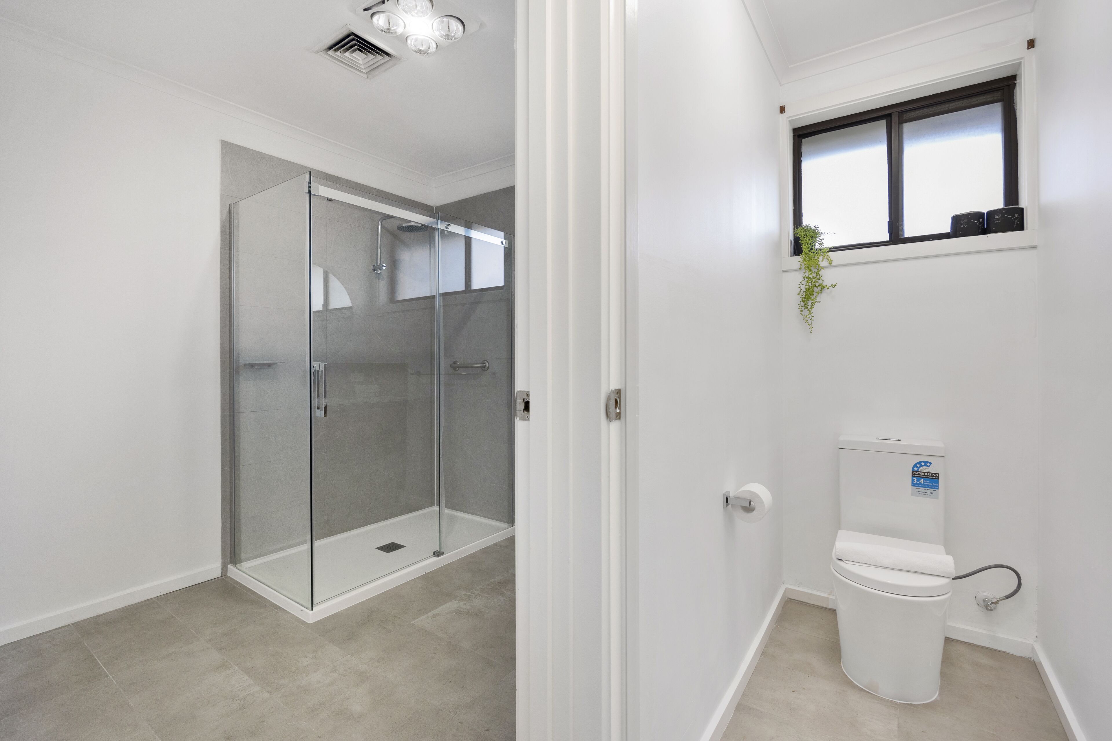 A bathroom with a glass-enclosed shower, a toilet, and a window with a plant.