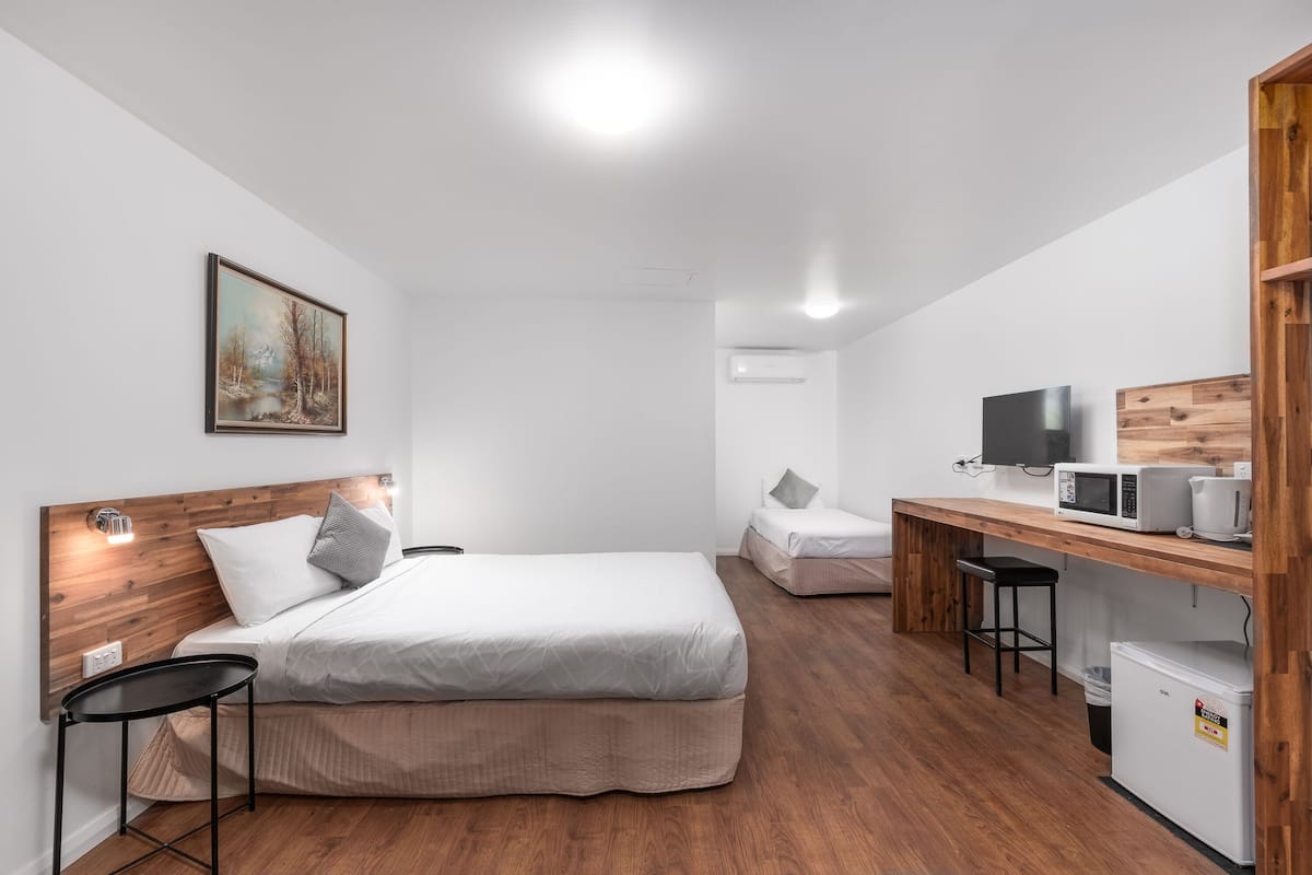 Ein modernes Hotelzimmer mit einem Holzkopfteil, einem Bett, einem Schreibtisch mit Computer, einer Mikrowelle und einem kleinen Kühlschrank.