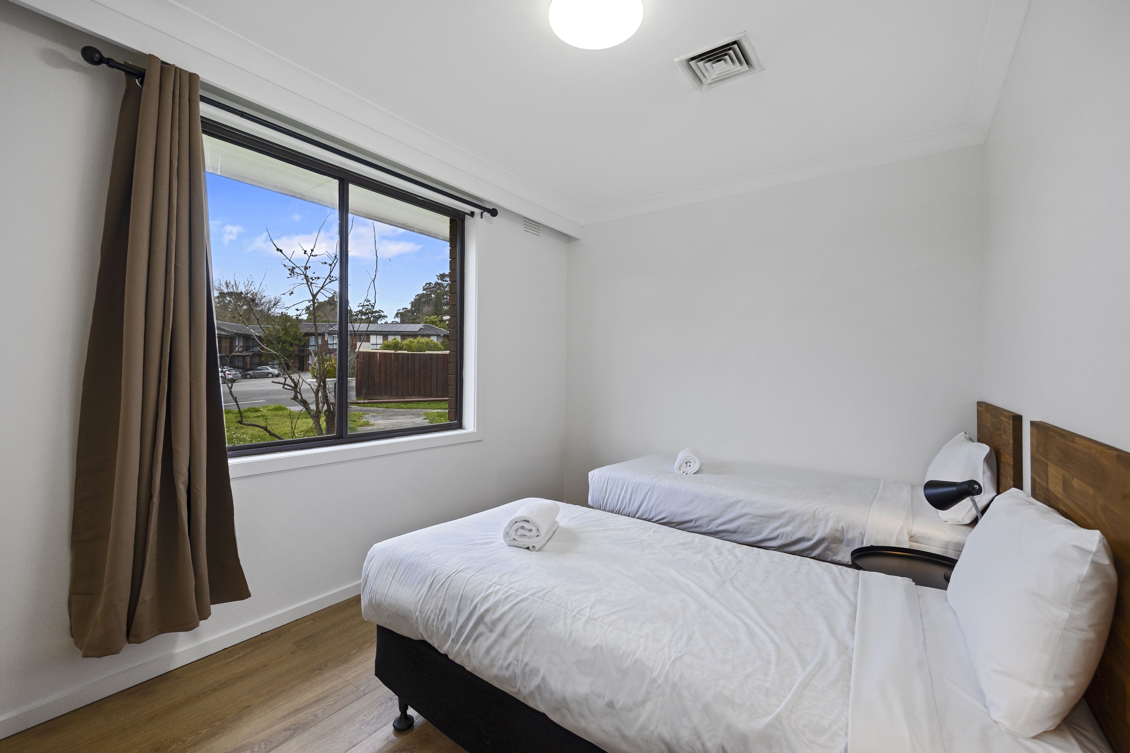 A bedroom with two beds, a window with curtains, and a view of the outside.