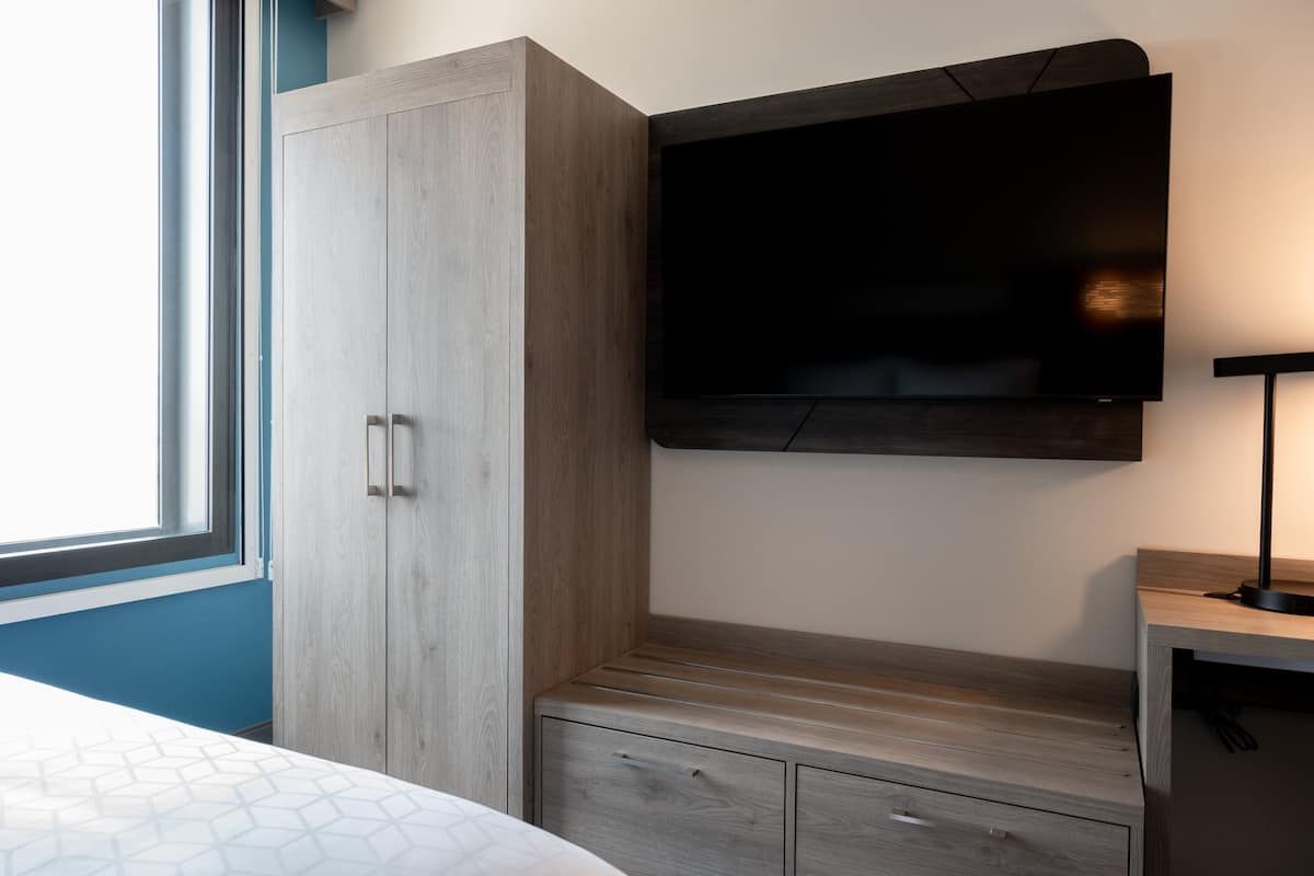 A bedroom with a bed, a wardrobe, a desk, and a TV mounted on the wall.
