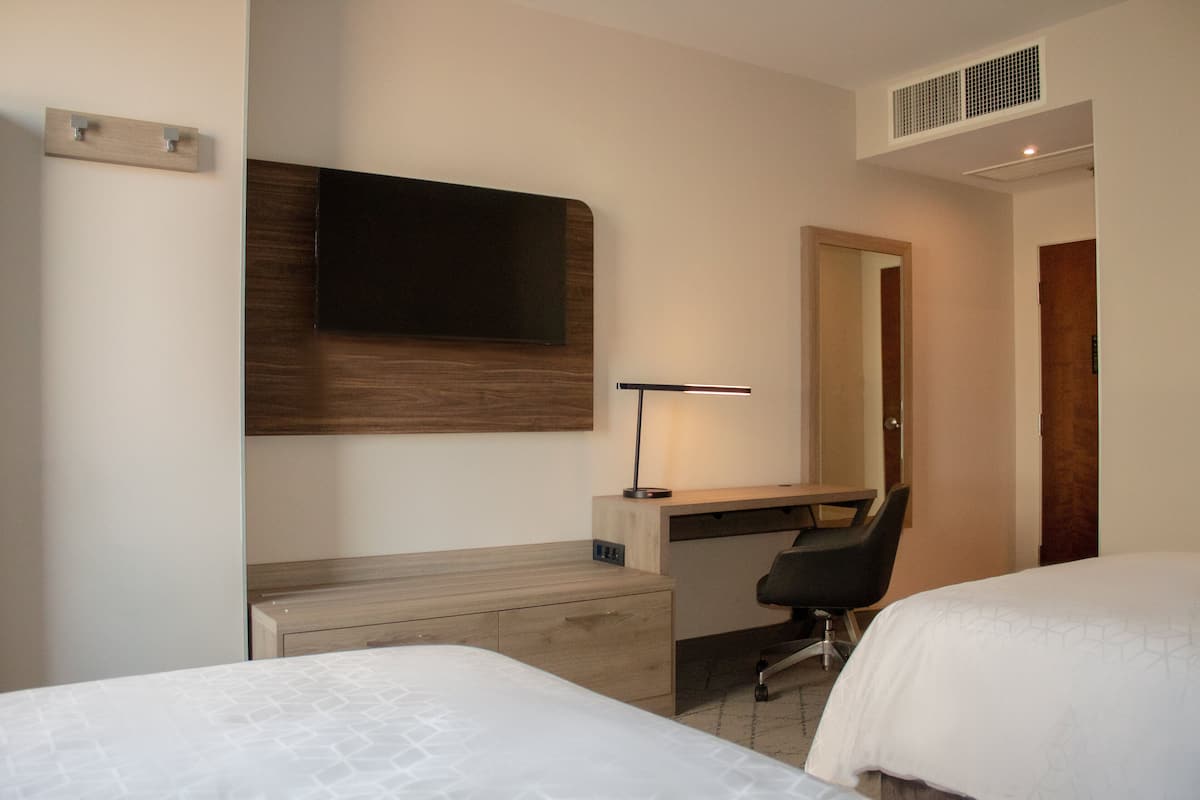 A hotel room with a bed, a desk with a chair, a TV mounted on the wall, and a mirror.
