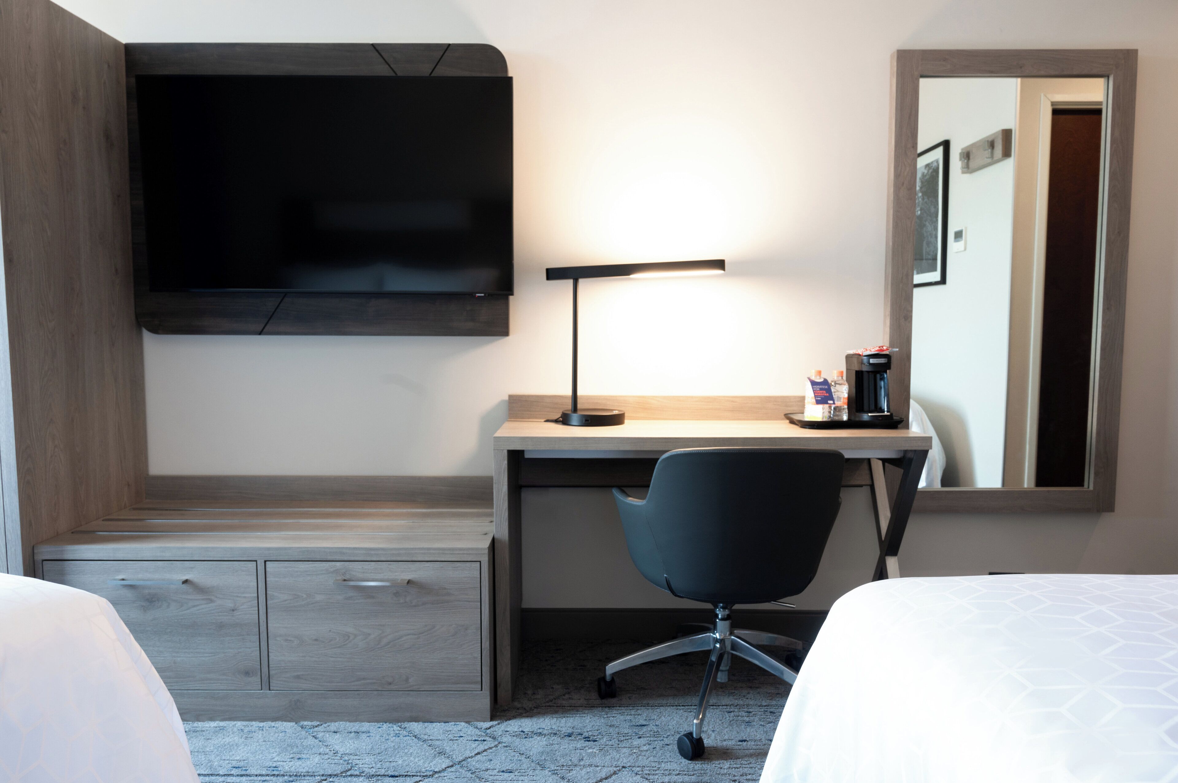 A hotel room with a bed, a desk with a chair, a TV mounted on the wall, and a coffee machine.