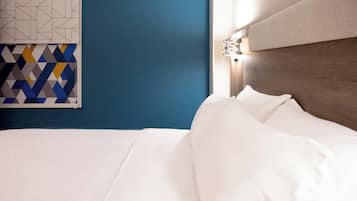 Una cama bien tendida con sábanas blancas en una habitación con pared azul y un tapiz de motivos geométricos.
