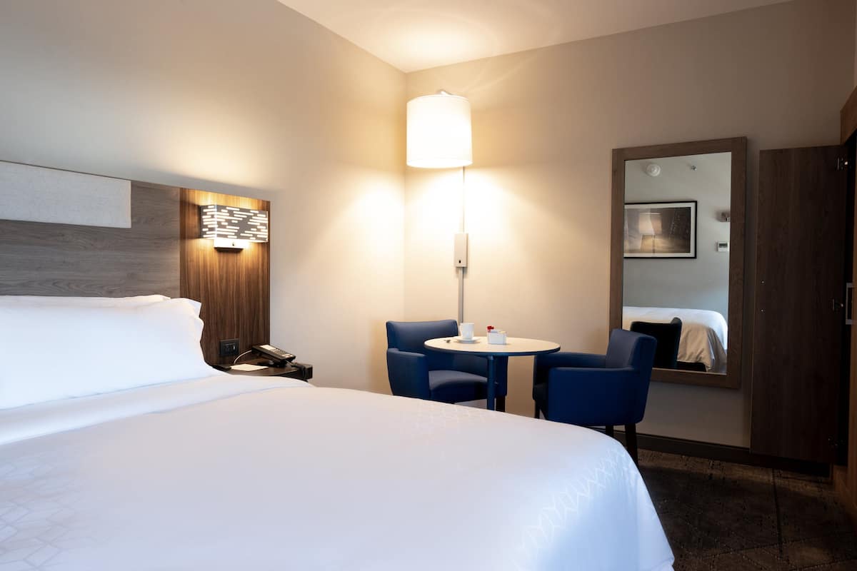 A hotel room with a large bed, a desk with a lamp, two chairs, and a small table.