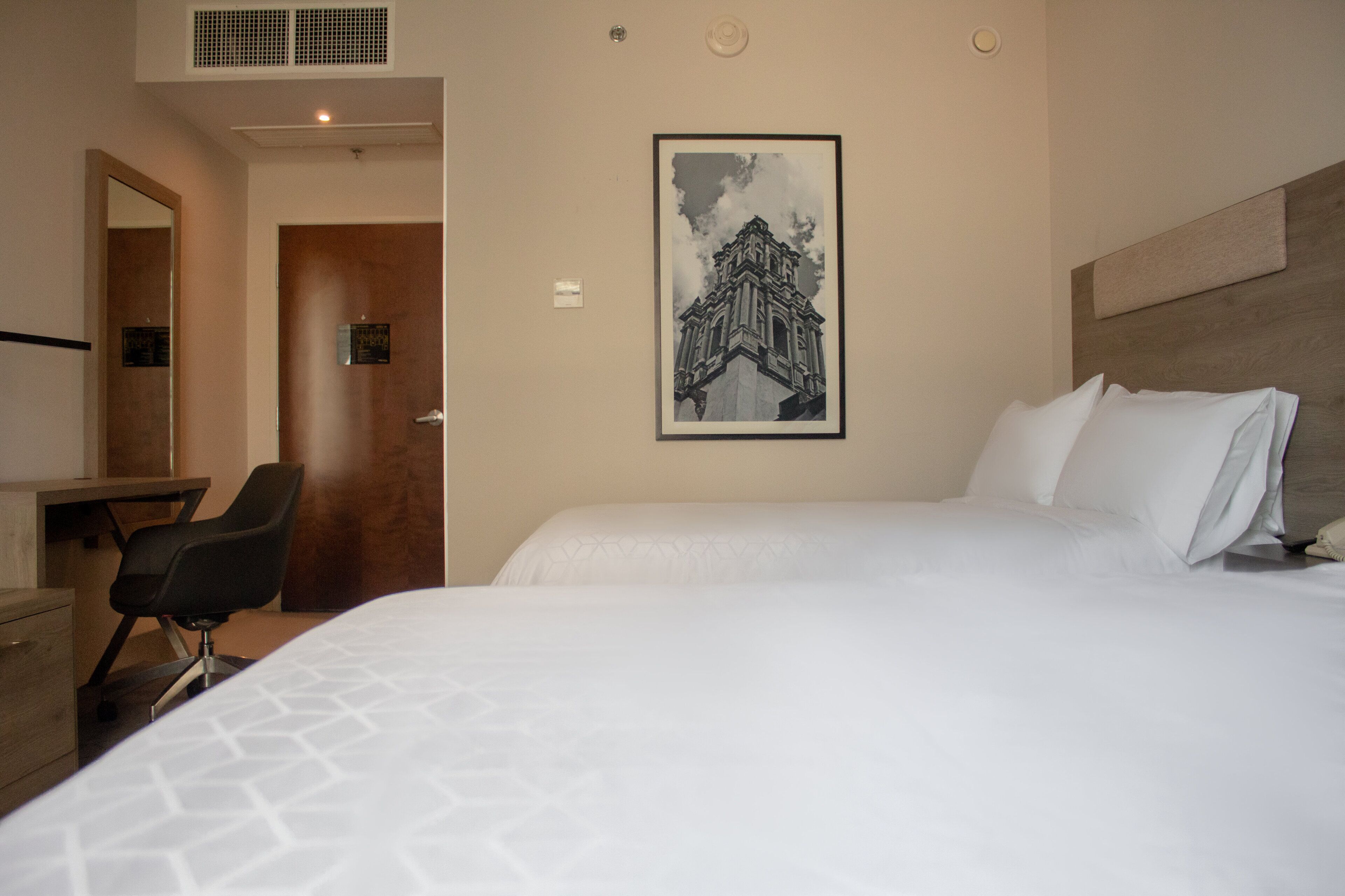Une chambre d’hôtel avec un grand lit, un bureau, une chaise et un tableau encadré au mur.