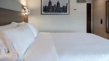Une chambre d’hôtel avec un grand lit, un tableau représentant une vue de la ville encadré au mur, une table de chevet avec une lampe et une porte dotée d’une serrure à carte magnétique.