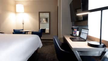 A hotel room with a bed, a desk with a laptop, a chair, a lamp, and a coffee machine.