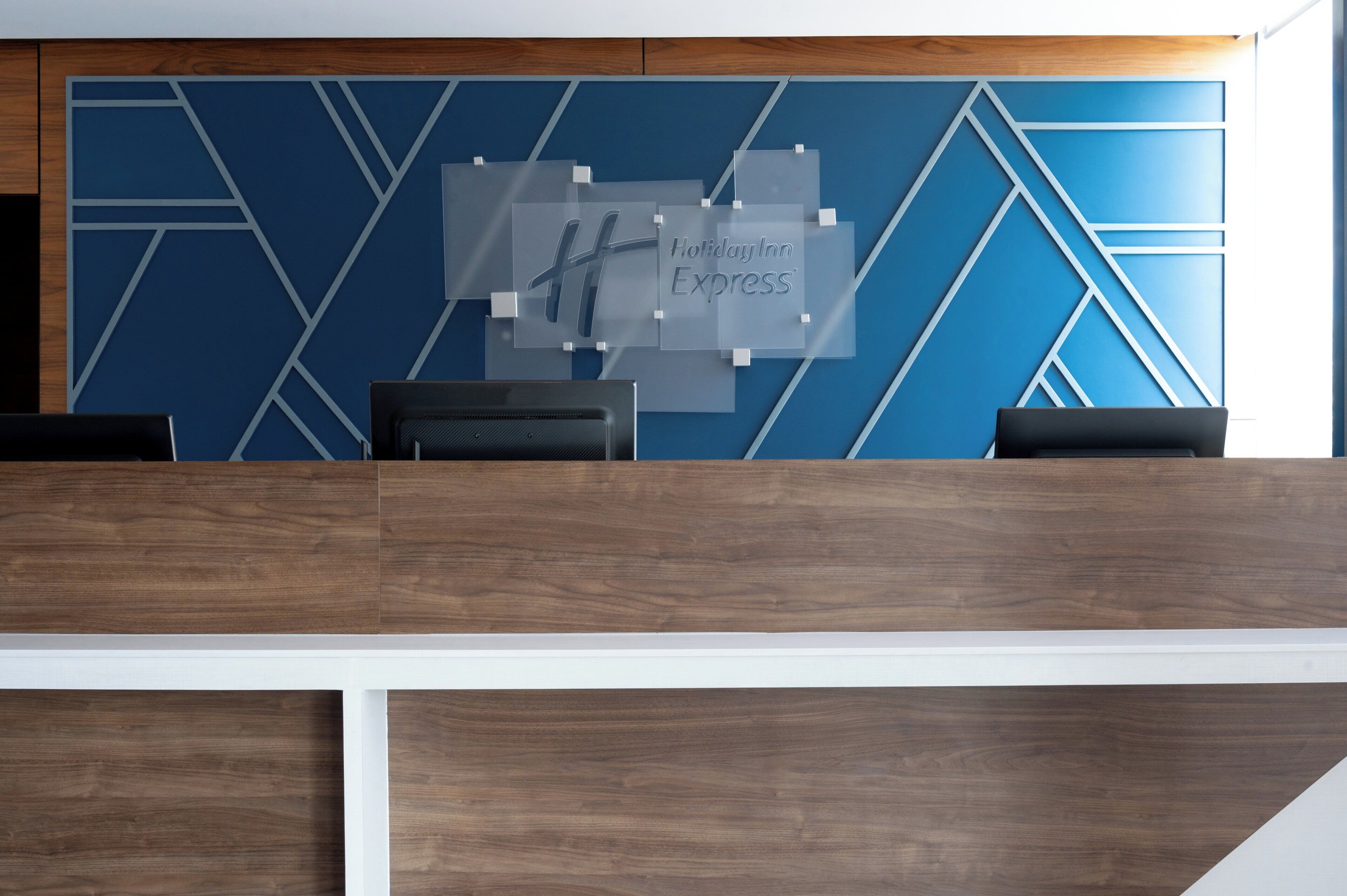 A reception desk with a blue geometric wall design and a sign that reads 'Holiday Inn Express'.