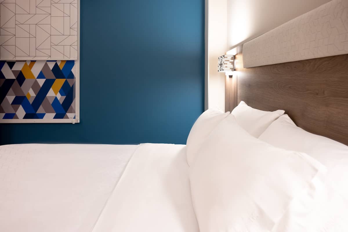 A neatly made bed with white linens, a wooden headboard, and a geometric-patterned wall art piece above it.