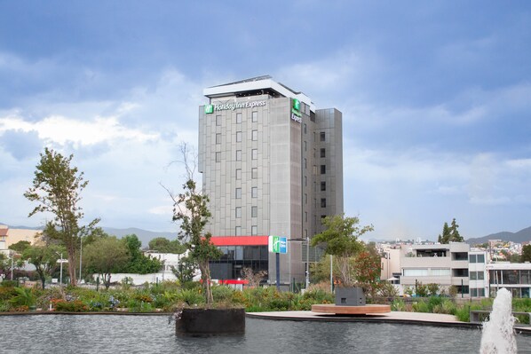 Un hotel Holiday Inn Express con un diseño moderno, situado cerca de una masa de agua con una fuente.