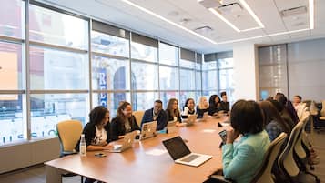 A conference room with a long table, laptops, and people seated around it.
