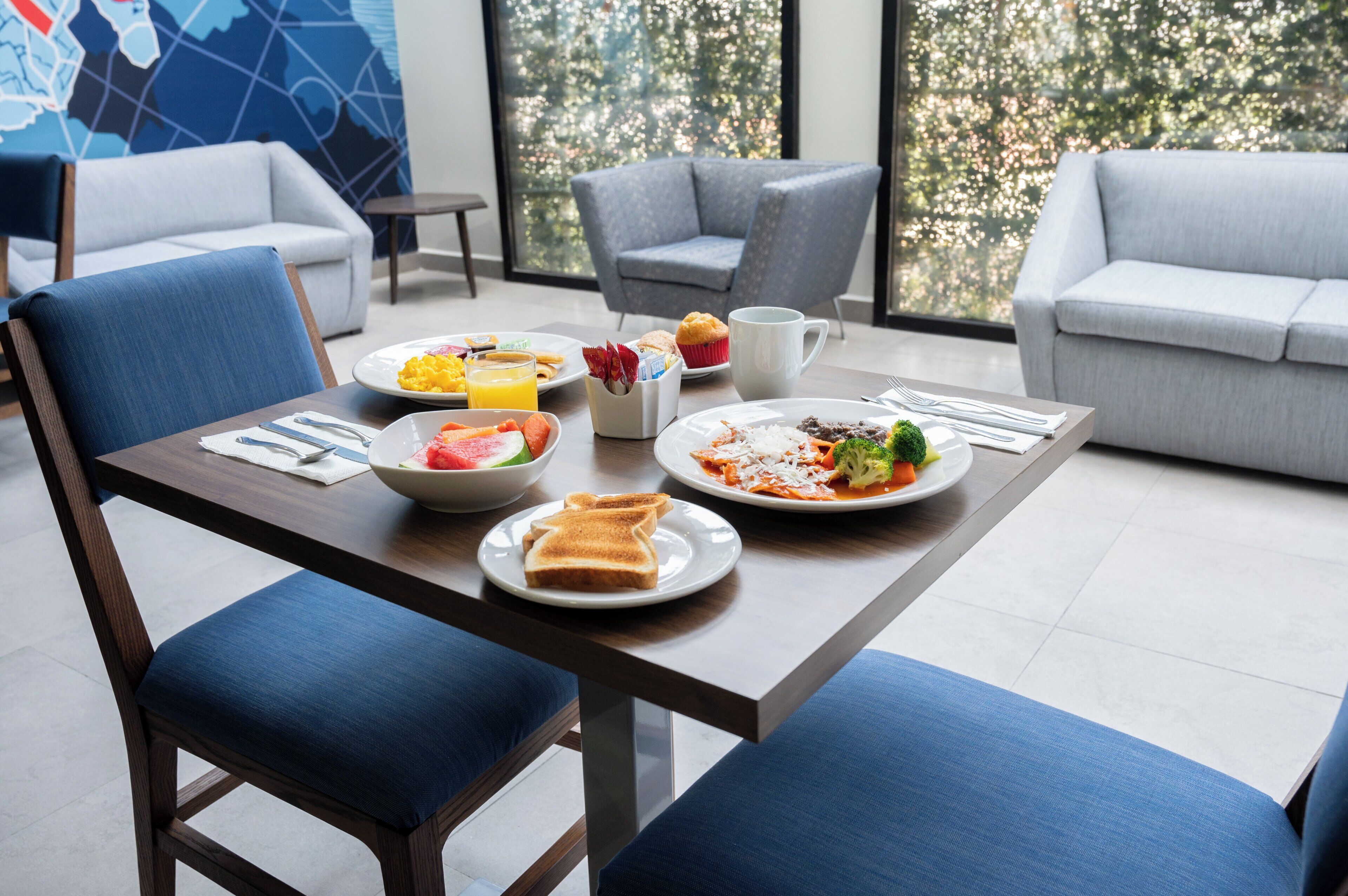 A dining area with a table set for breakfast, including plates of food, a muffin, and a cup.
