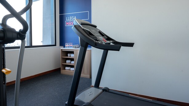 A treadmill in a room with a large window, a wall with a motivational message, and a shelf with towels. - Holiday Inn Express Mexico City Satelite by IHG (Naucalpan)