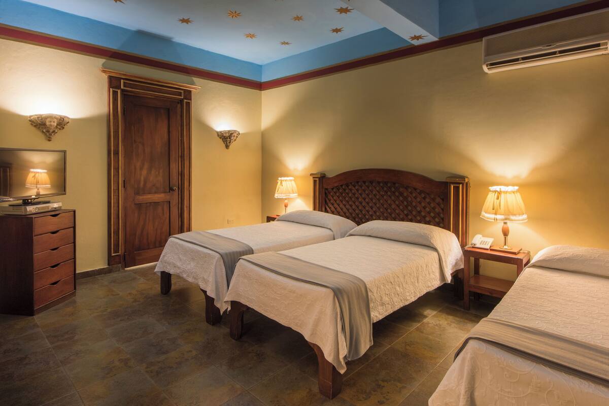 A hotel room with two beds, a wooden wardrobe, a desk with a lamp, and a ceiling with star decorations.