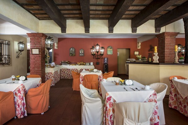 A dining area with tables set for a meal, featuring a brick column and wall-mounted lanterns.