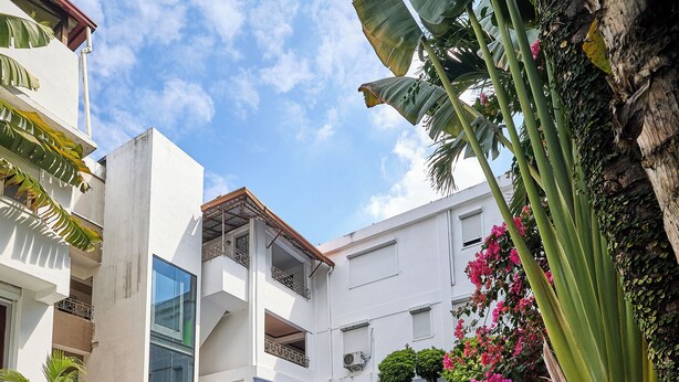 A pool area with a covered seating area, surrounded by lush greenery and a multi-story building with balconies. - Hotel San Marco (Santo Domingo)