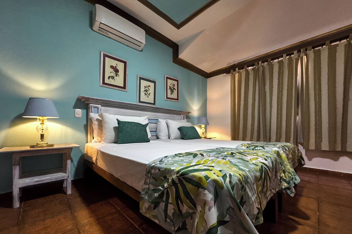 A neatly made bed with a floral bedspread, a bedside lamp, and framed pictures on the wall.