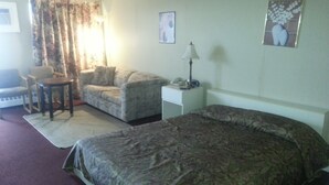 A hotel room with a bed, a sofa, a chair, a small table, a lamp, and a painting on the wall. - Newburg Inn Motel (Township of Wilmot)