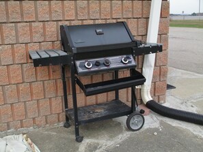 A portable grill with a control panel and a lower shelf, set against a brick wall.