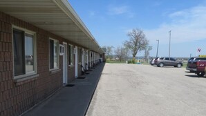 A motel with a row of rooms along a brick wall, a parking lot, and a clear blue sky. - Newburg Inn Motel (Township of Wilmot)