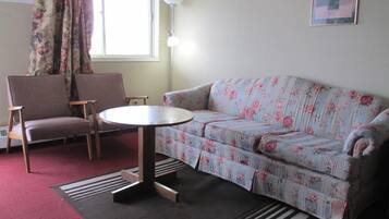 Una sala de estar con un sofá floral, dos sillones, una mesa de centro redonda, una lámpara y una ventana con cortinas.