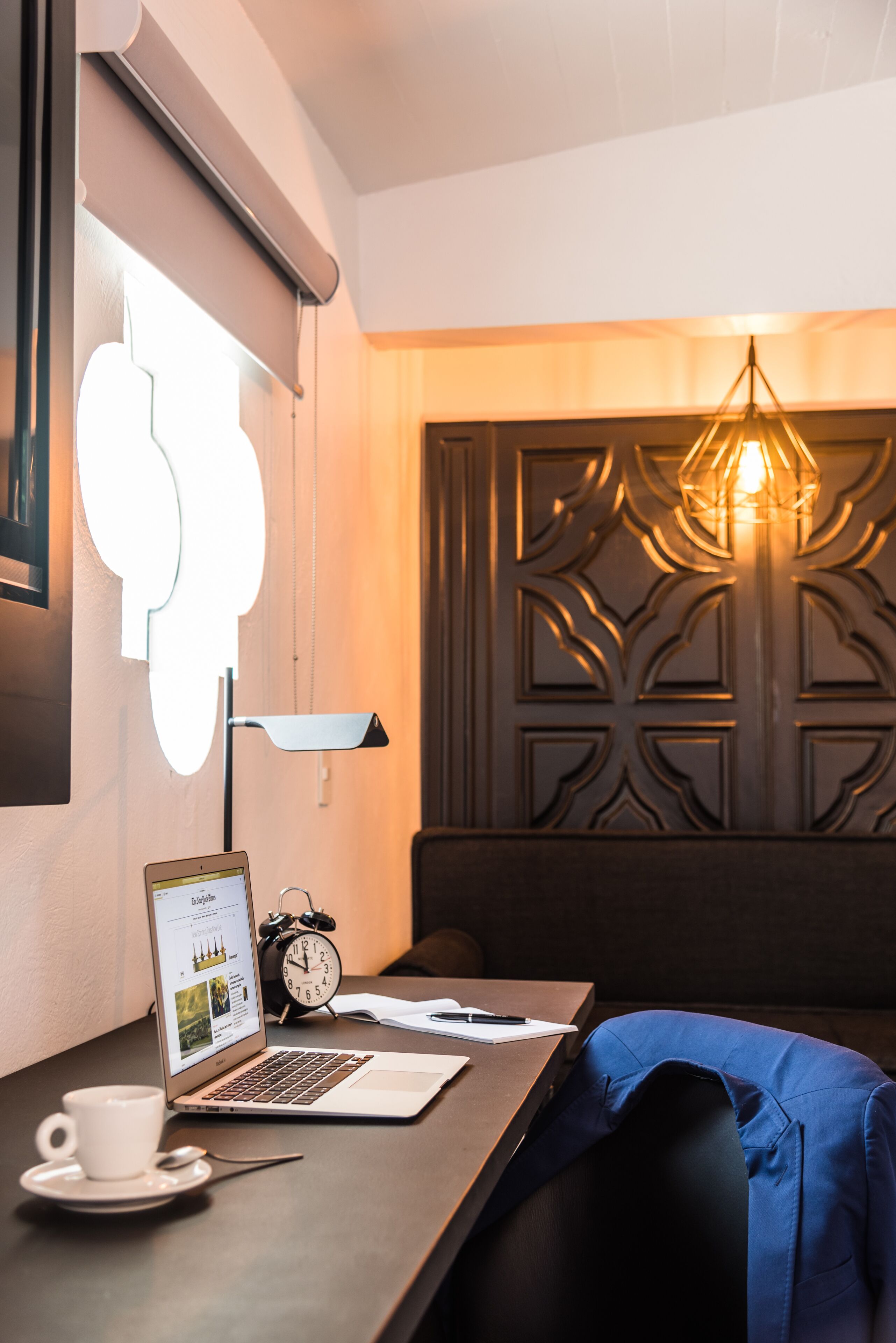 Una habitación moderna con una computadora portátil sobre una mesa, una taza, un reloj y un panel decorativo en la pared.