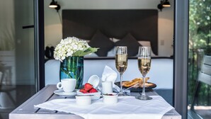 Una mesa con mantel blanco, dos copas de champán, un jarrón con flores blancas, una taza, un plato de fresas y una servilleta.