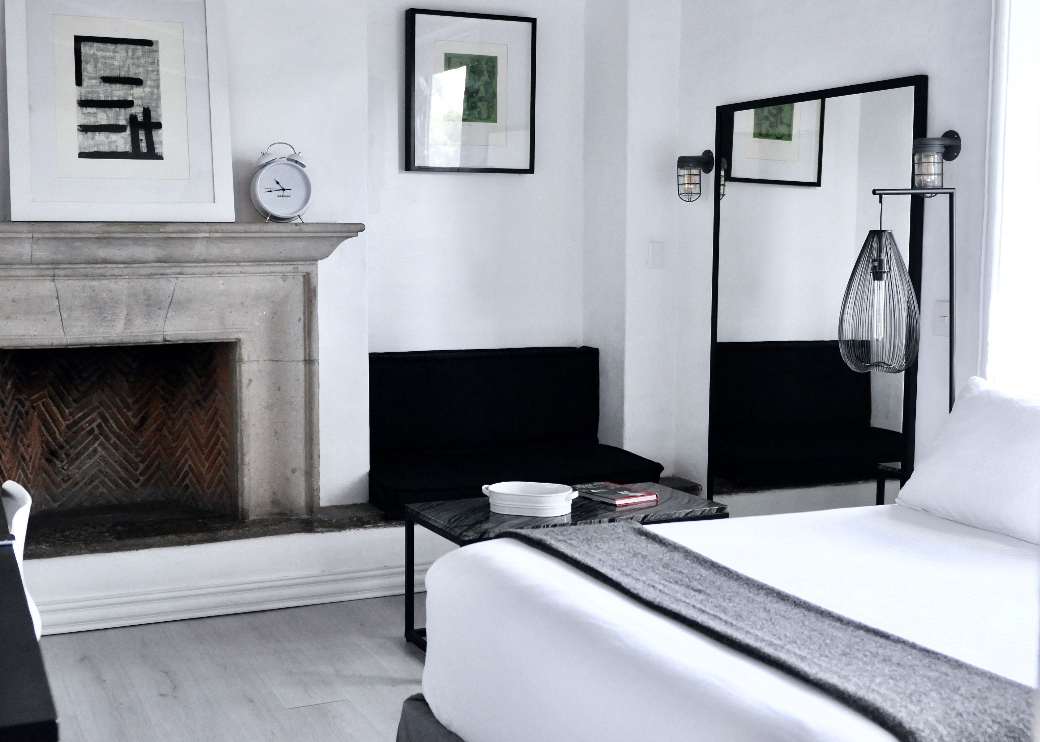A modern hotel room with a fireplace, a bed, a bedside table, a nightstand, a lamp, and framed artwork on the walls.