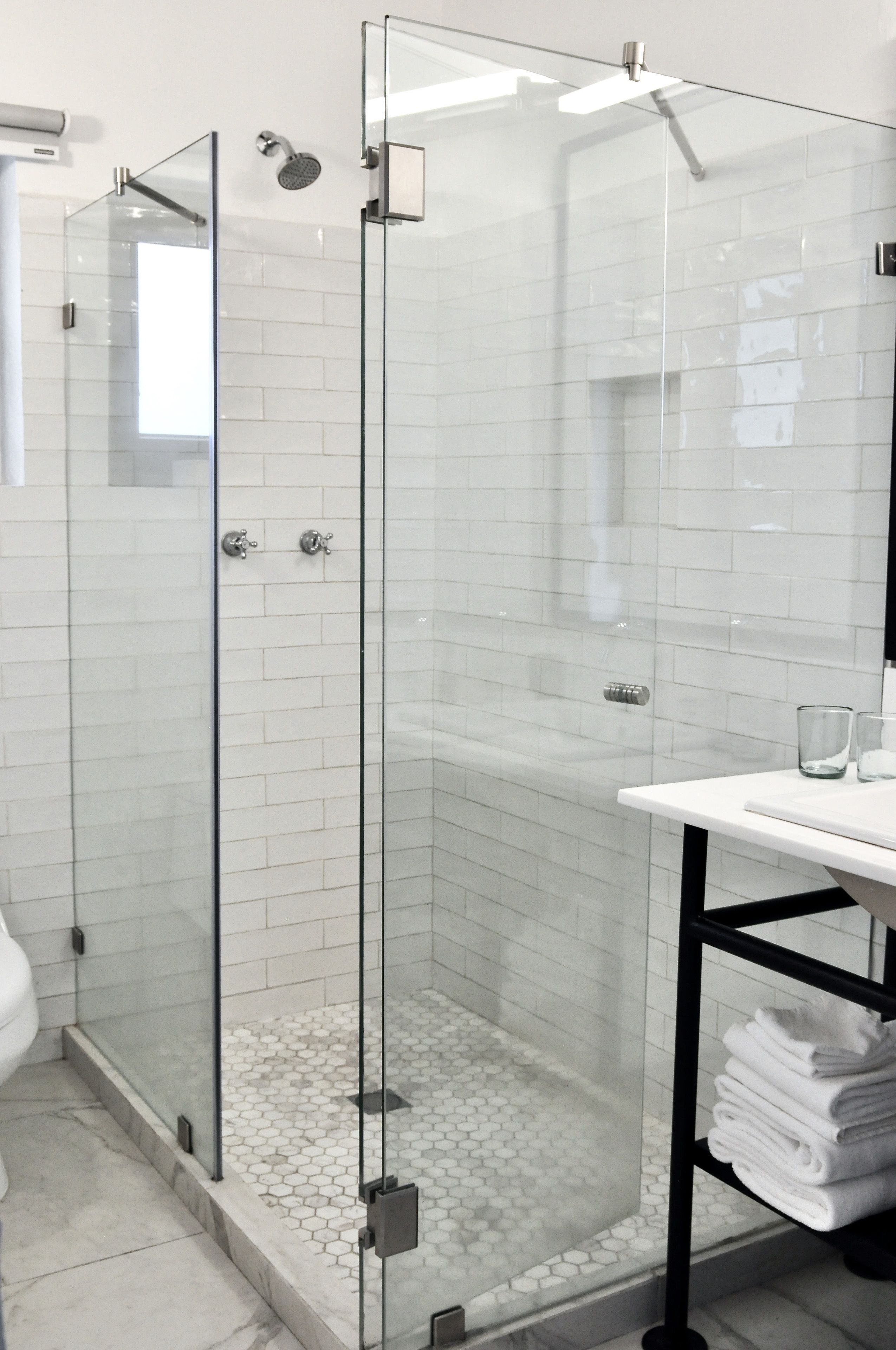 A modern bathroom with a glass-enclosed shower, white tiled walls, and a white sink with a towel rack.