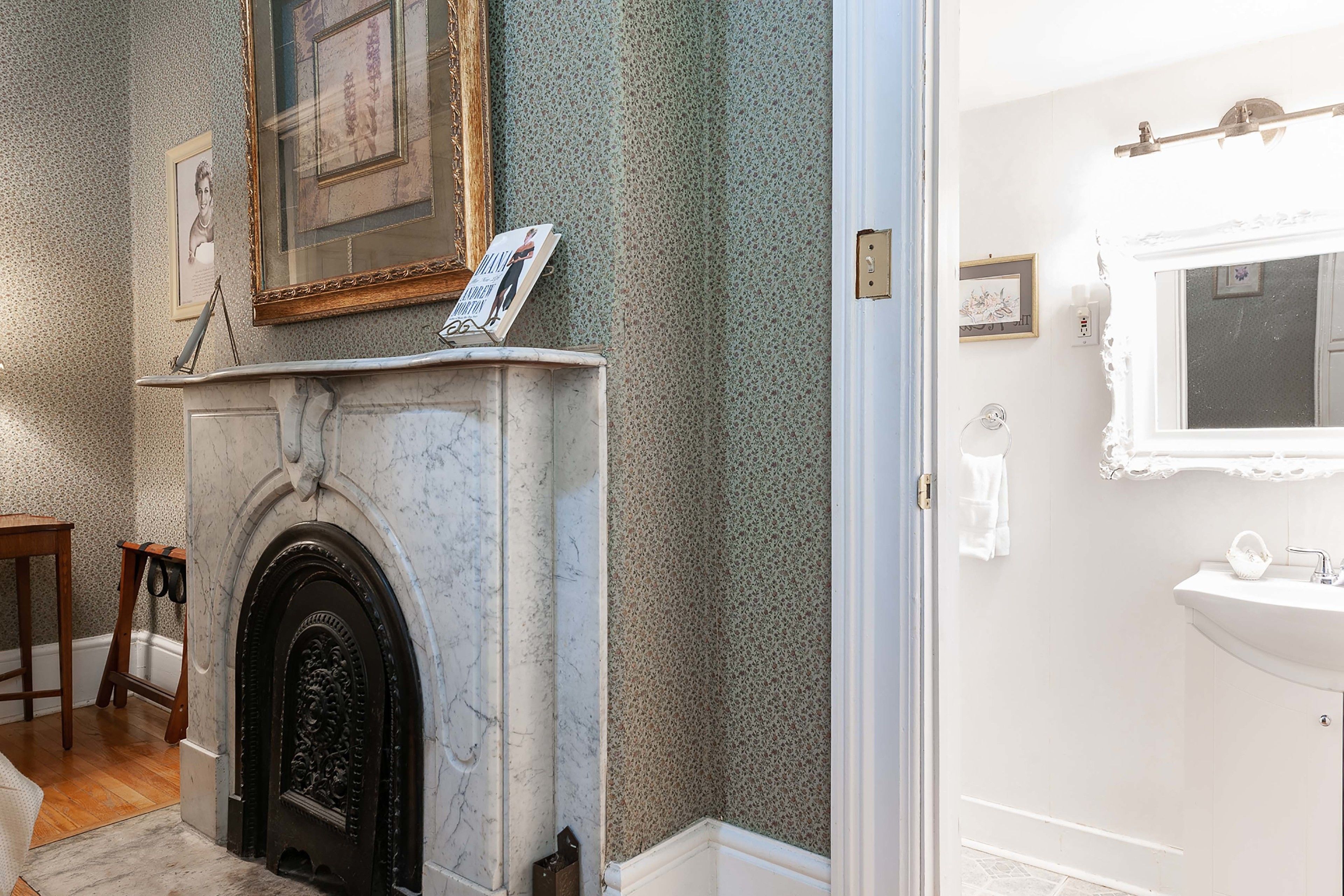 Une salle de bain avec une cheminée en marbre, un lavabo et des œuvres d’art encadrées accrochées au mur.