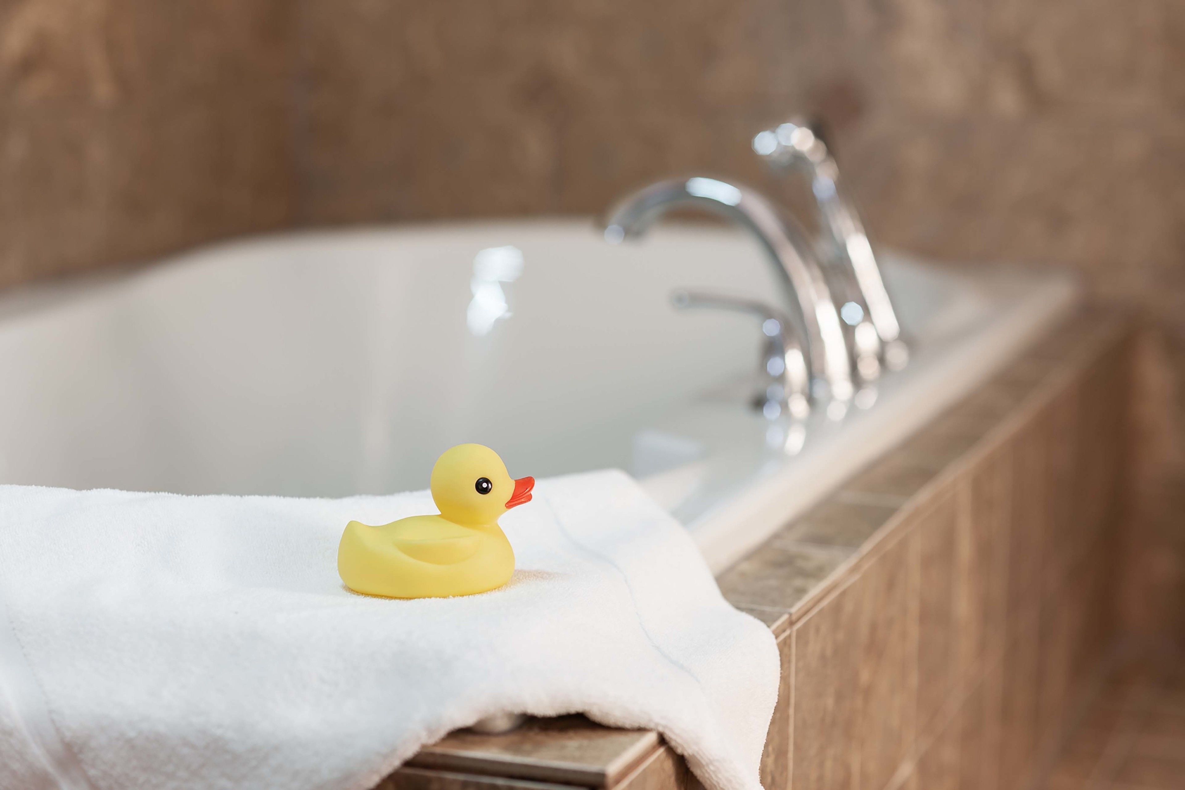 A bathtub with a yellow rubber duck and a white towel.