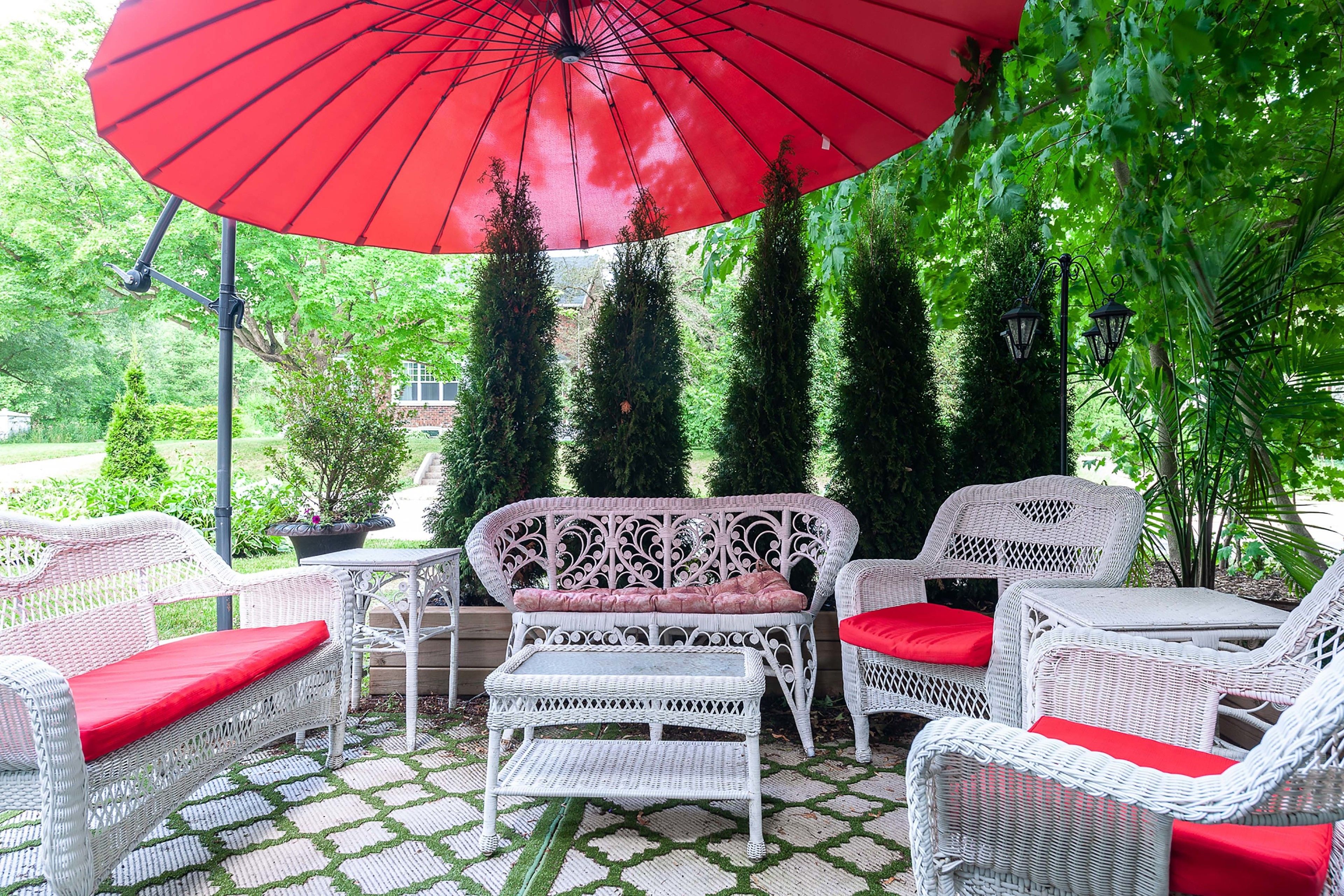 Une terrasse avec des meubles en osier, un parasol rouge et de la verdure.