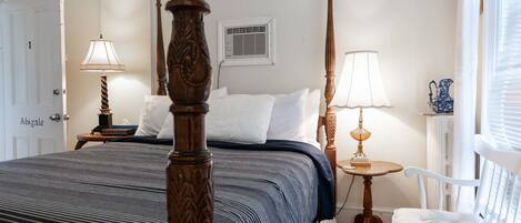 A bedroom with a four-poster bed, a bedside table with a lamp, a chair, and a radiator.