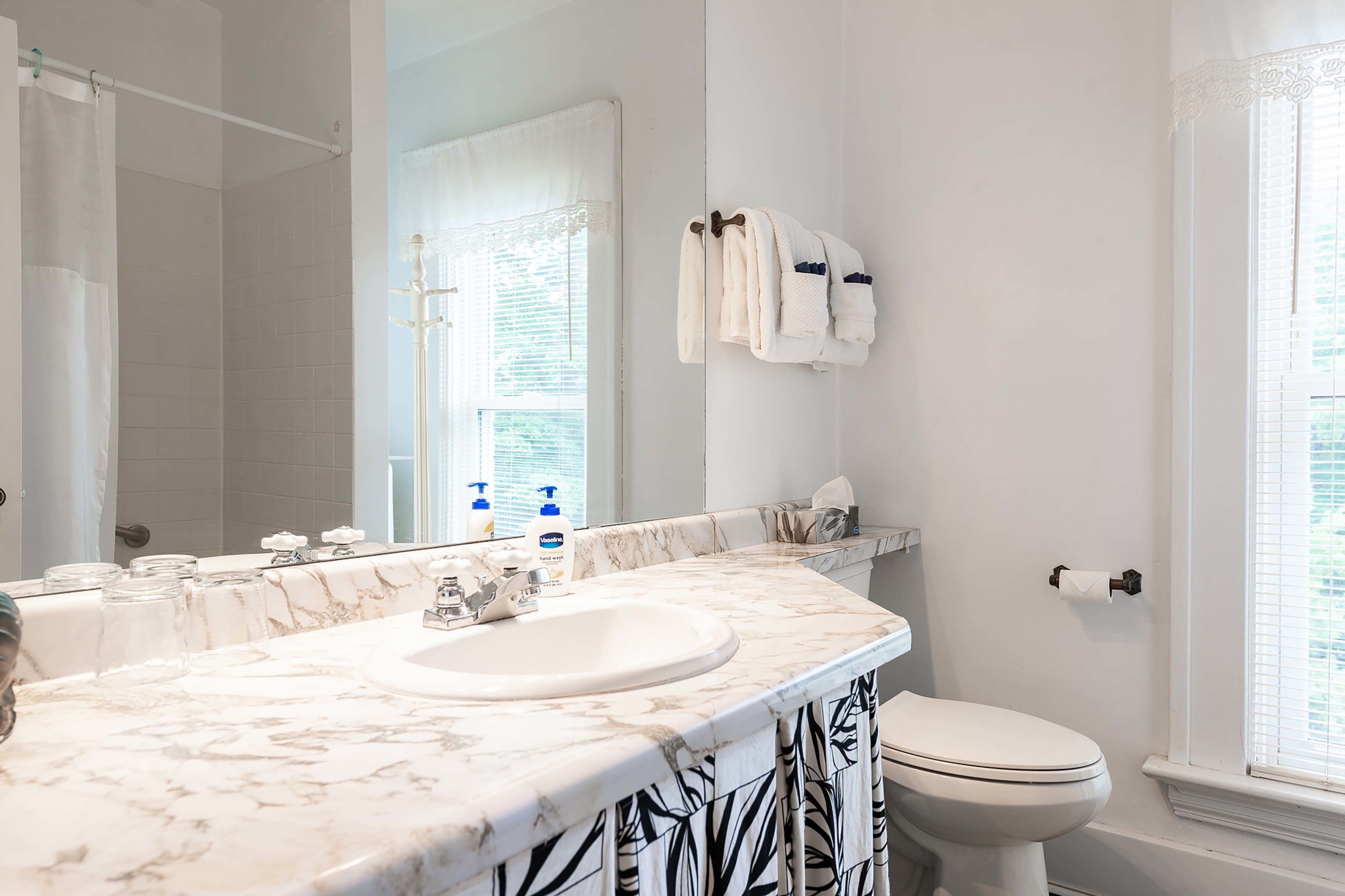 A bathroom with a marble sink, a toilet, a shower curtain, and a towel rack.