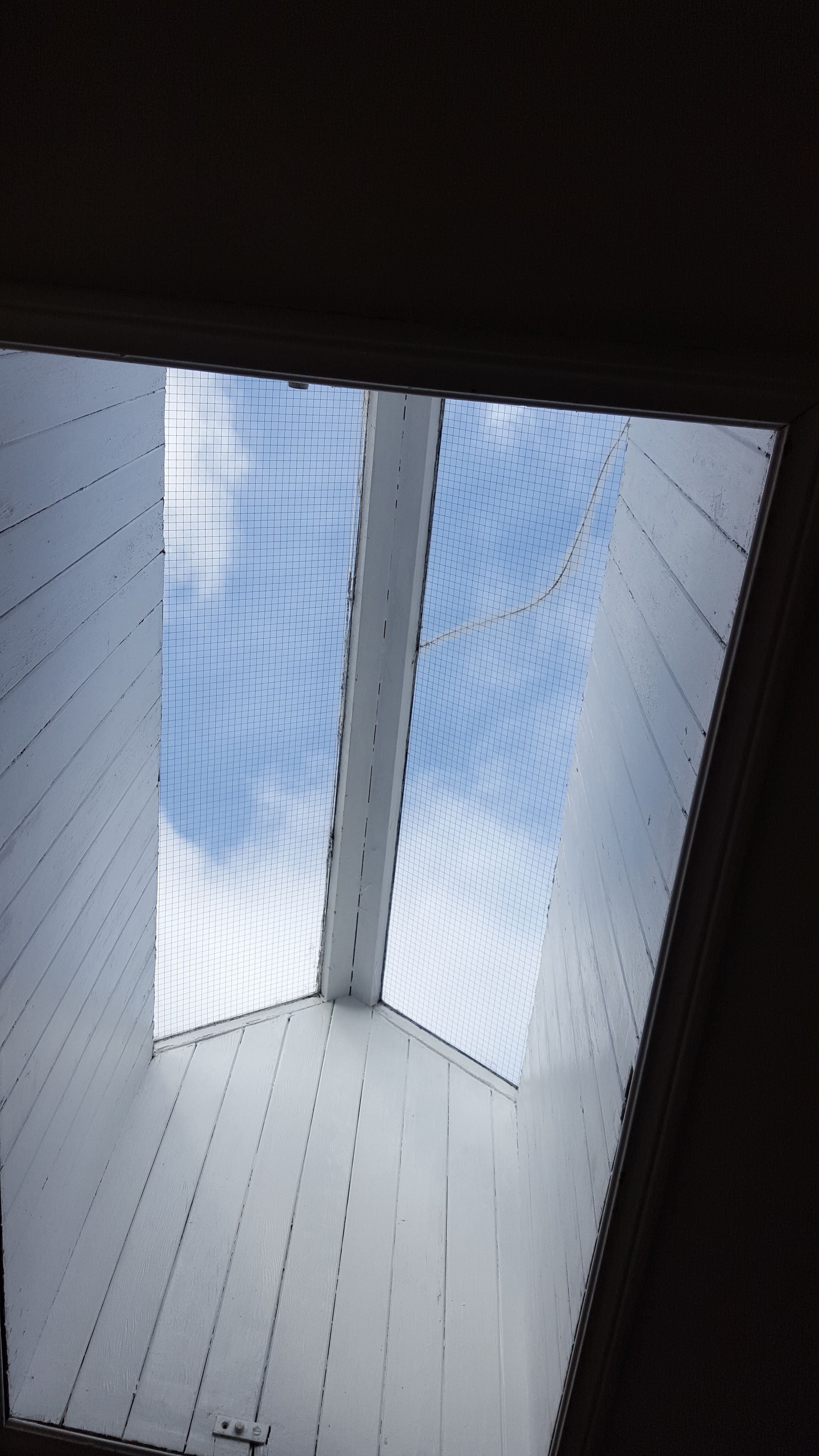 A skylight with a grid pattern, allowing natural light into a room with white wooden walls.