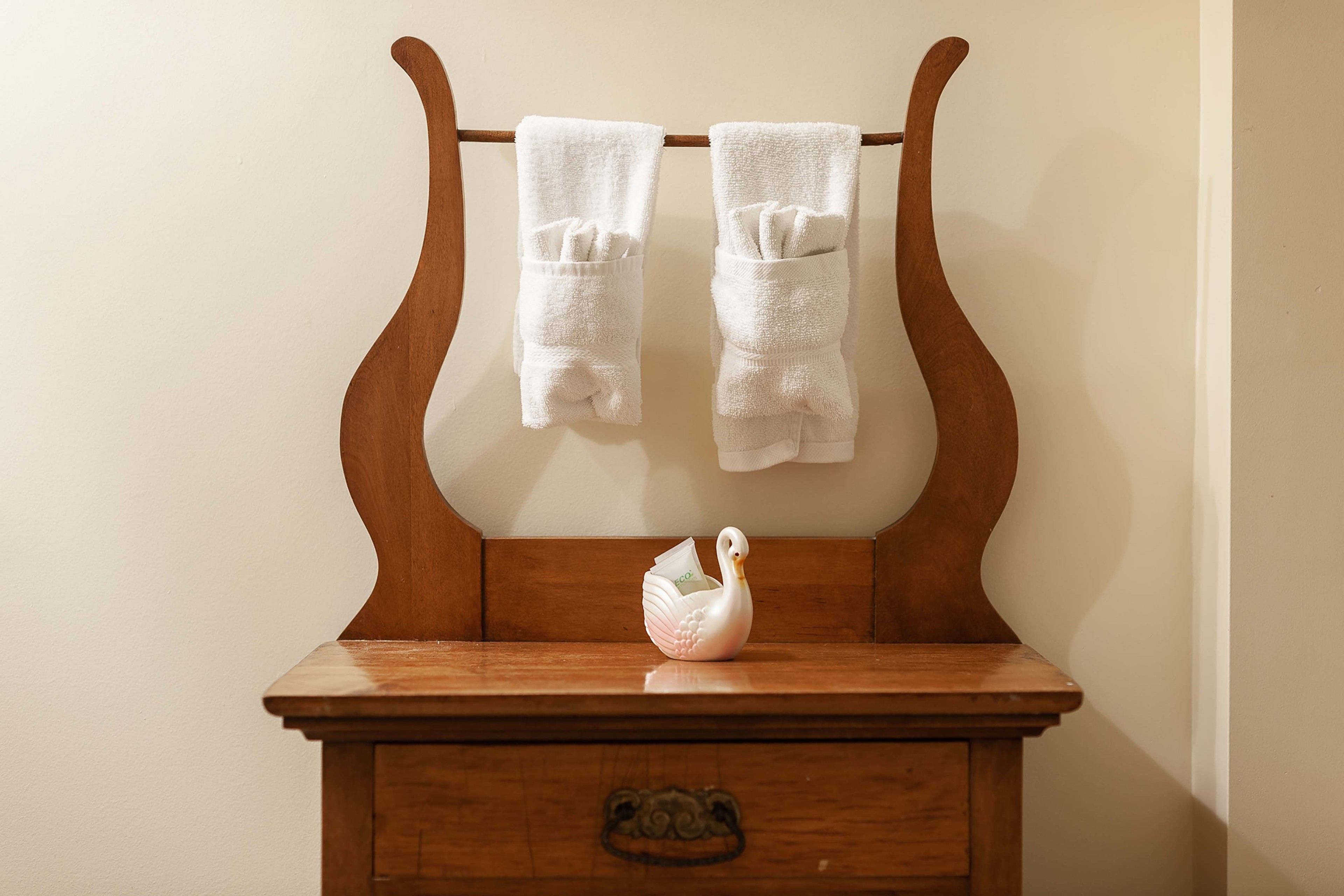 A wooden dresser with two white towels hanging on a wooden towel rack above it and a white swan-shaped soap dish on the dresser.