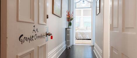 A hallway with white doors, a radiator, and a bed with a white and black patterned bedspread.