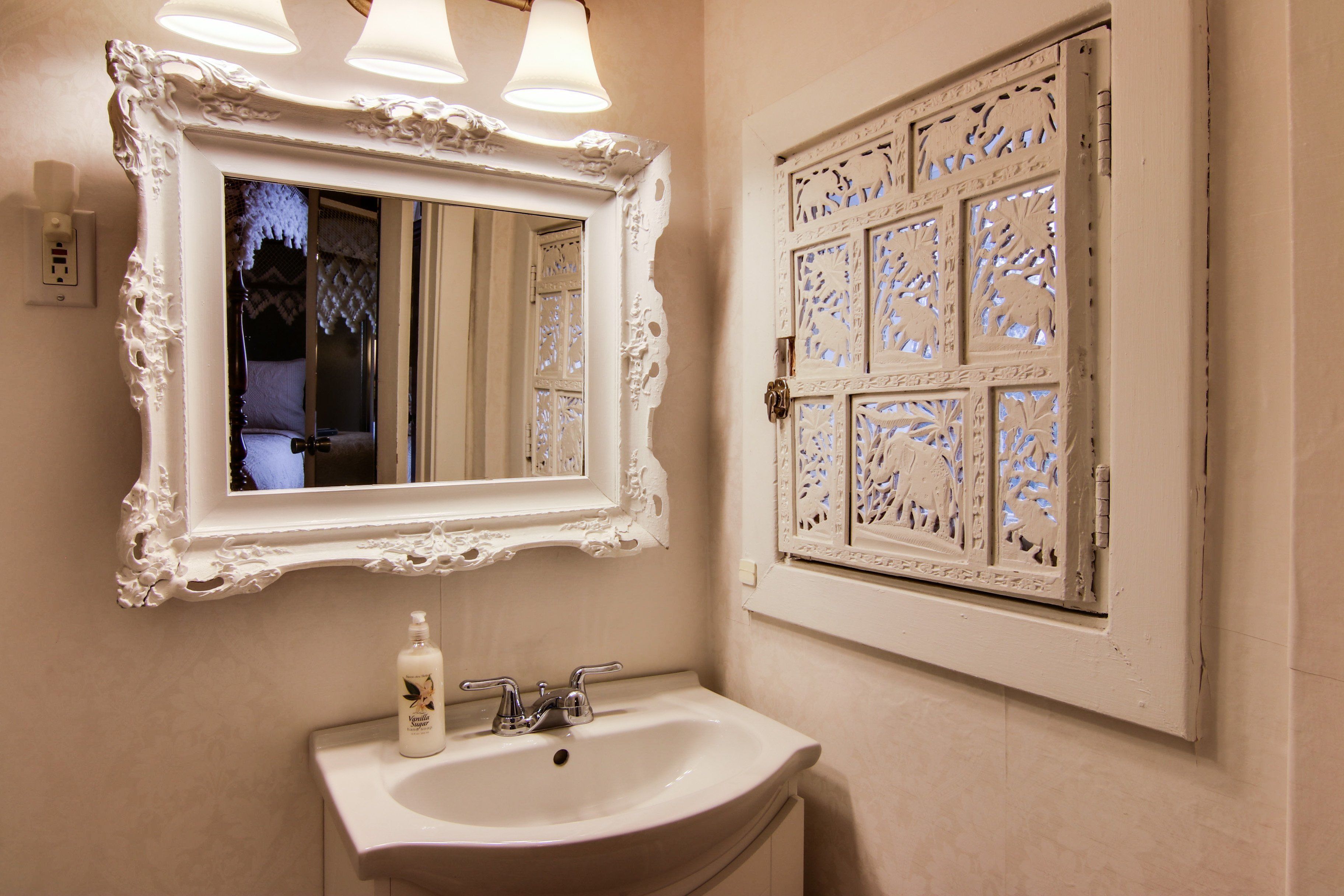 A bathroom with a white sink, a mirror with an ornate frame, and a decorative window with intricate patterns.