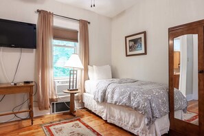 A bedroom with a bed, a TV mounted on the wall, a window with curtains, a bedside table, and a framed picture on the wall.