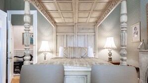 A bedroom with a bed, two chairs, a nightstand, a lamp, and a framed picture on the wall.
