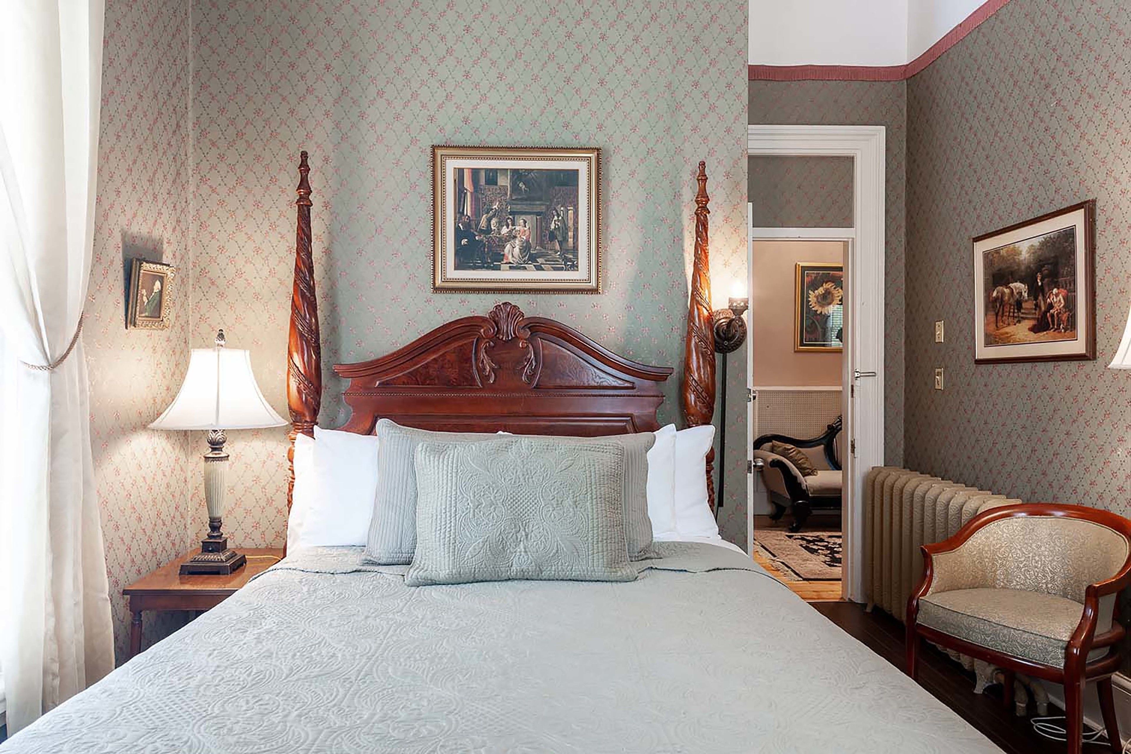A bedroom with a large bed, a wooden headboard, a nightstand with a lamp, and a chair.
