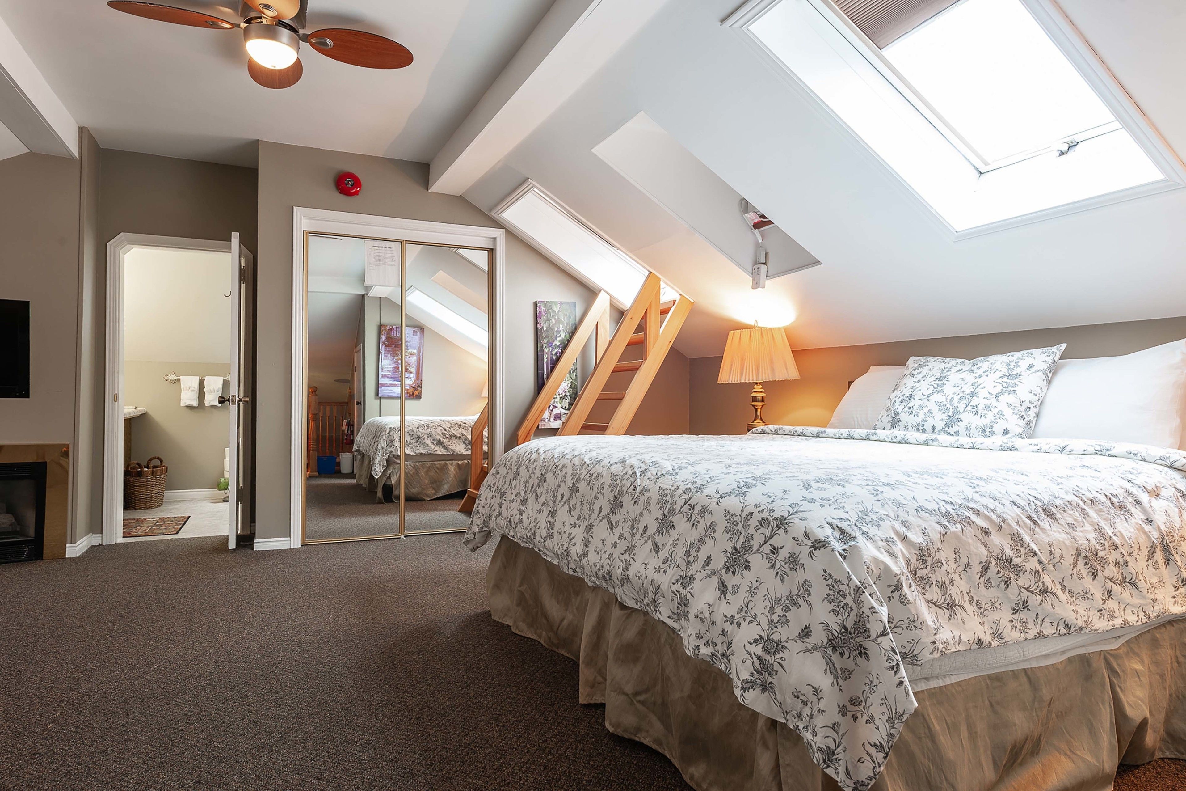 A bedroom with a large bed, skylight, ceiling fan, and a staircase leading to an upper level.